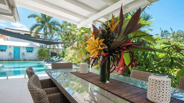 A glass-top dining table with wicker chairs, a vase of flowers, and a decorative lantern. - Paradise on Ruby - Port Douglas (Port Douglas)