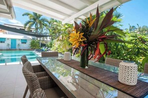 A glass-top dining table with wicker chairs, a vase of flowers, and a decorative lantern. - Paradise on Ruby - Port Douglas (Port Douglas)