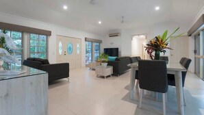 A spacious living area with a modern design, featuring a glass coffee table, black sofas, a dining table with chairs, and decorative plants. - Paradise on Ruby - Port Douglas (Port Douglas)