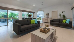 A spacious living area with two dark sofas, a coffee table, and large windows offering a view of the outdoors. - Paradise on Ruby - Port Douglas (Port Douglas)