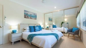 A modern bedroom with a large bed, a nightstand, a chair, and a mirror. - Paradise on Ruby - Port Douglas (Port Douglas)