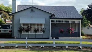 A single-story house with a gabled roof, a front porch with a railing, and a garage door. - Fairway Views Accomadation (Warragul)