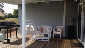 A covered patio with a grill, two wicker chairs with colorful cushions, and a small table. - Fairway Views Accomadation (Warragul)