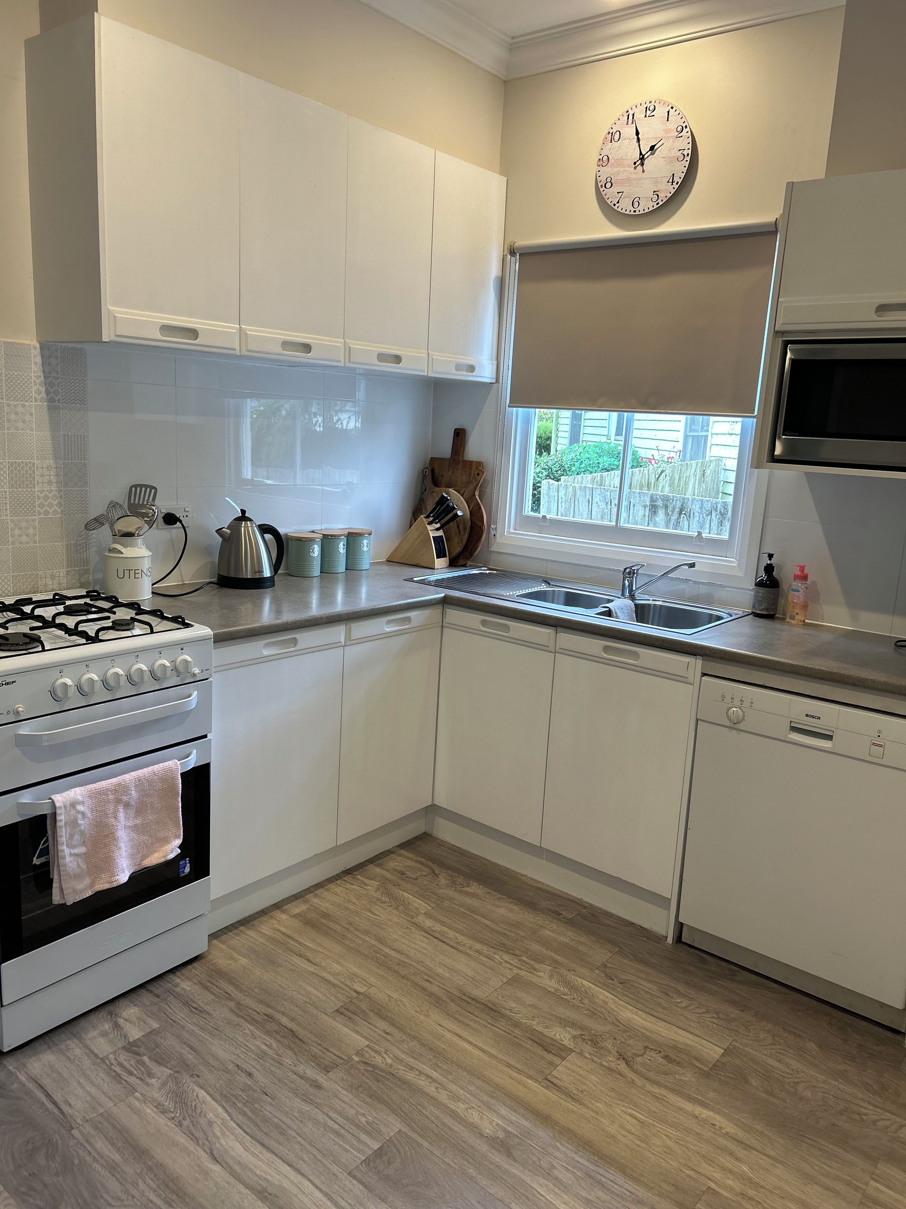 Una cocina moderna con armarios blancos, una estufa a gas, un lavavajillas Bosch y una ventana con vistas al exterior.