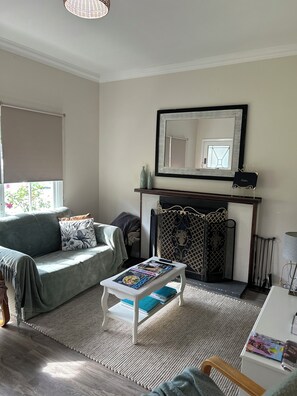 A living room with a sofa, a small table with magazines, a fireplace, and a large mirror.