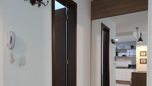 Un pasillo con suelo de madera, una puerta que da a una zona de cocina y un teléfono instalado en la pared.