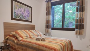 Una cama bien hecha con ropa de cama a rayas, un cabecero de madera, una mesita de noche pequeña y una ventana con cortinas.