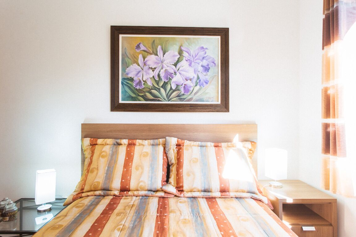 Une chambre d’hôtel avec un lit, une table de chevet, une lampe et un tableau représentant des fleurs, accroché au mur.