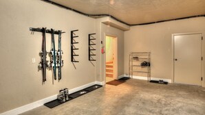 A room with a concrete floor, a wall-mounted ski rack, a metal shoe rack, and a door leading to another room. - Reduced January Rates!  Great Location. 5starReviews. 3 Bed, 2 Bath with Views (Park City)