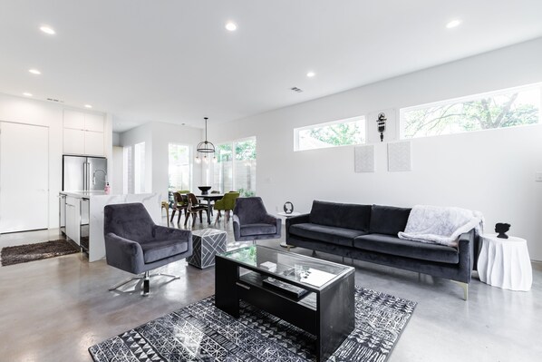 Ein modernes Wohnzimmer mit einem dunkelgrauen Sofa, einem Glastisch und einem gemusterten Teppich.
