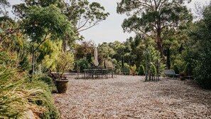 Un espace extérieur aménagé avec des tables et des chaises, entouré d’arbres et de plantes.