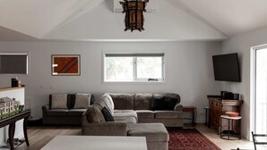 A living room with a sectional sofa, a flat-screen TV, a window, and a decorative wall piece.
