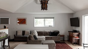 Uma sala de estar com sofá modular, televisão de tela plana, janela e um objeto decorativo na parede.