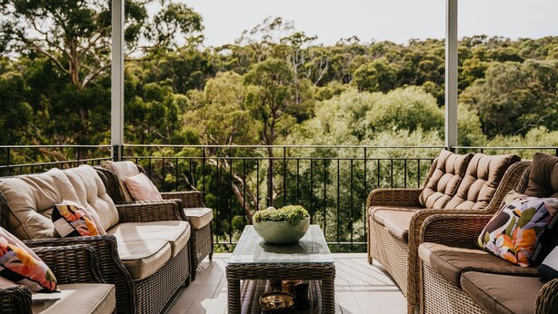 A balcony with wicker furniture, a table with a potted plant, and a view of dense greenery.