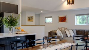 A modern kitchen with a dining area, a living room with a sofa and chairs, and artwork on the walls.