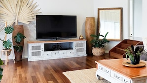 Un salon doté d’un téléviseur à écran plat, d’un meuble de rangement en bois et de diverses plantes.