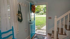 Una puerta con marco verde azulado, un timbre blanco y una bolsa verde colgando de un gancho.