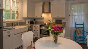 Una cocina con armarios blancos, estufa, horno, lavamanos y una mesa de comedor con un jarrón de flores.