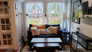 Una sala de estar con un sofá, dos sillones, una mesa de centro y un televisor sobre un mueble.