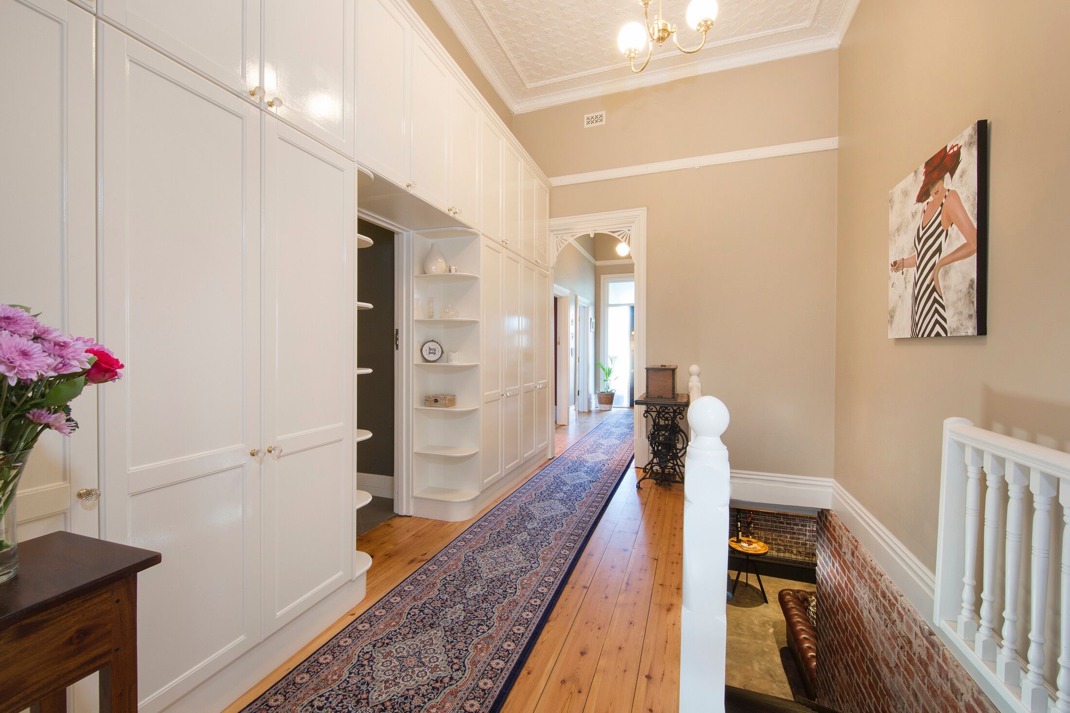 A hallway with white cabinets, a patterned rug, and a staircase with a white railing.