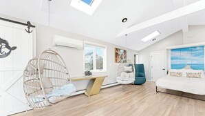 A modern bedroom with a sloped ceiling, a bed, two hanging chairs, a desk, and a view of the sky through a skylight.