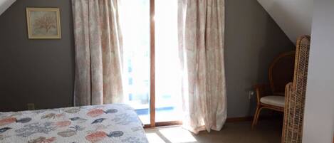 Un dormitorio con cama, una silla y ventana con cortinas.