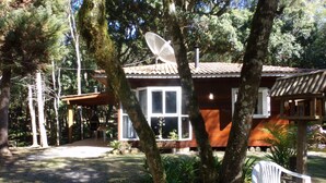 Una casa con antena parabólica, terraza de madera y una silla de plástico blanco.
