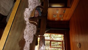 Un interior de madera con una escalera, un cortinaje de encaje y un ventanal con vistas a árboles.
