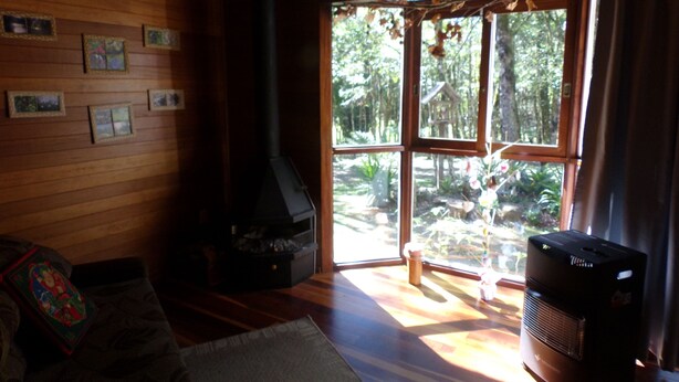 Un salón acogedor con paredes de madera, chimenea y un amplio ventanal con vistas al exterior.