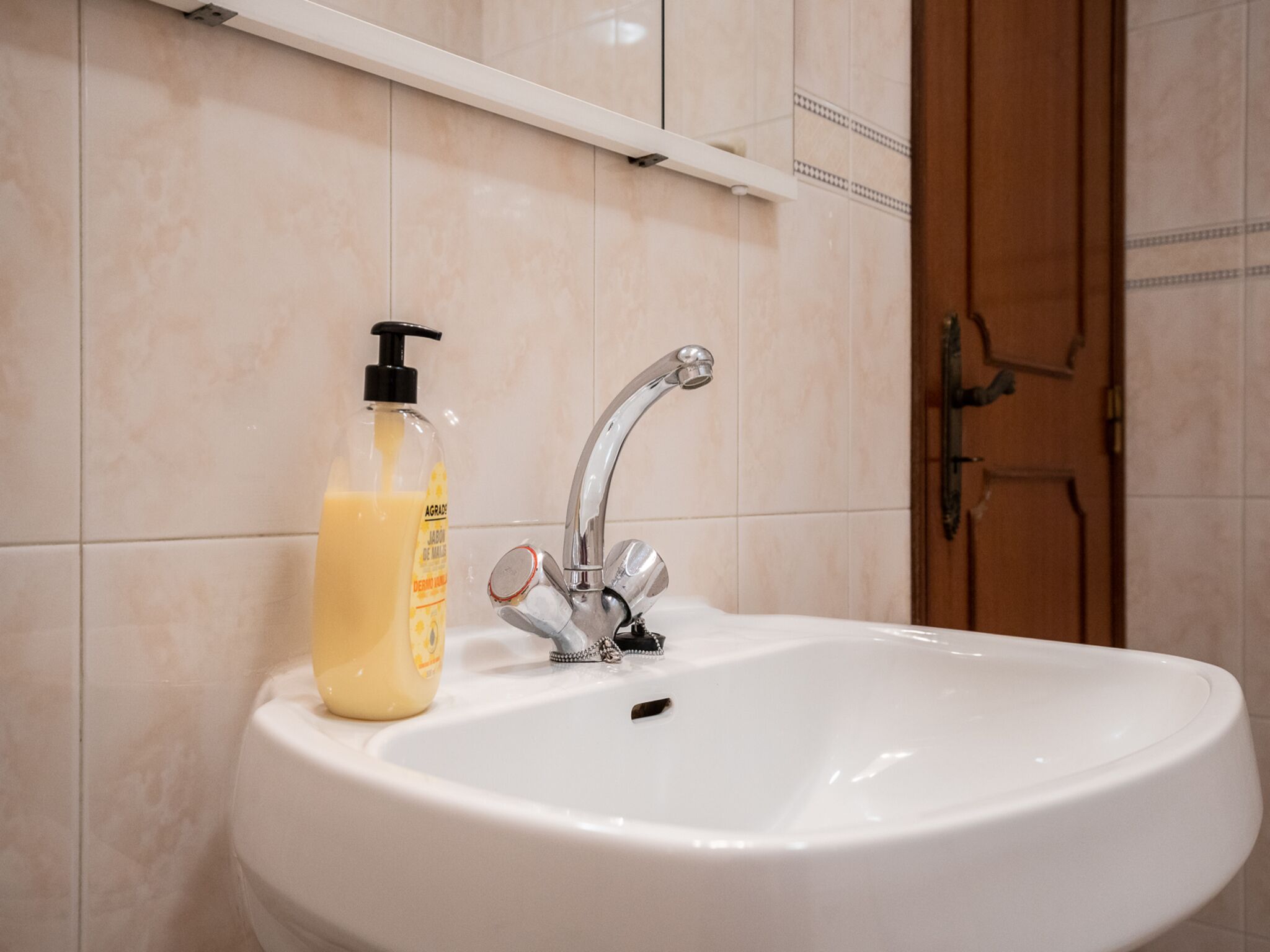 A bathroom with a white sink, a silver faucet, and a bottle of liquid soap.