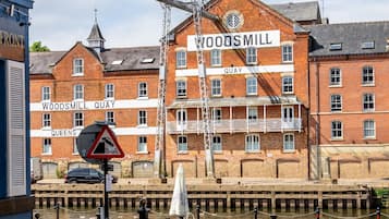 A historic building named Woodmill Quay with a prominent sign, a canal in front, and a pedestrian bridge overhead.