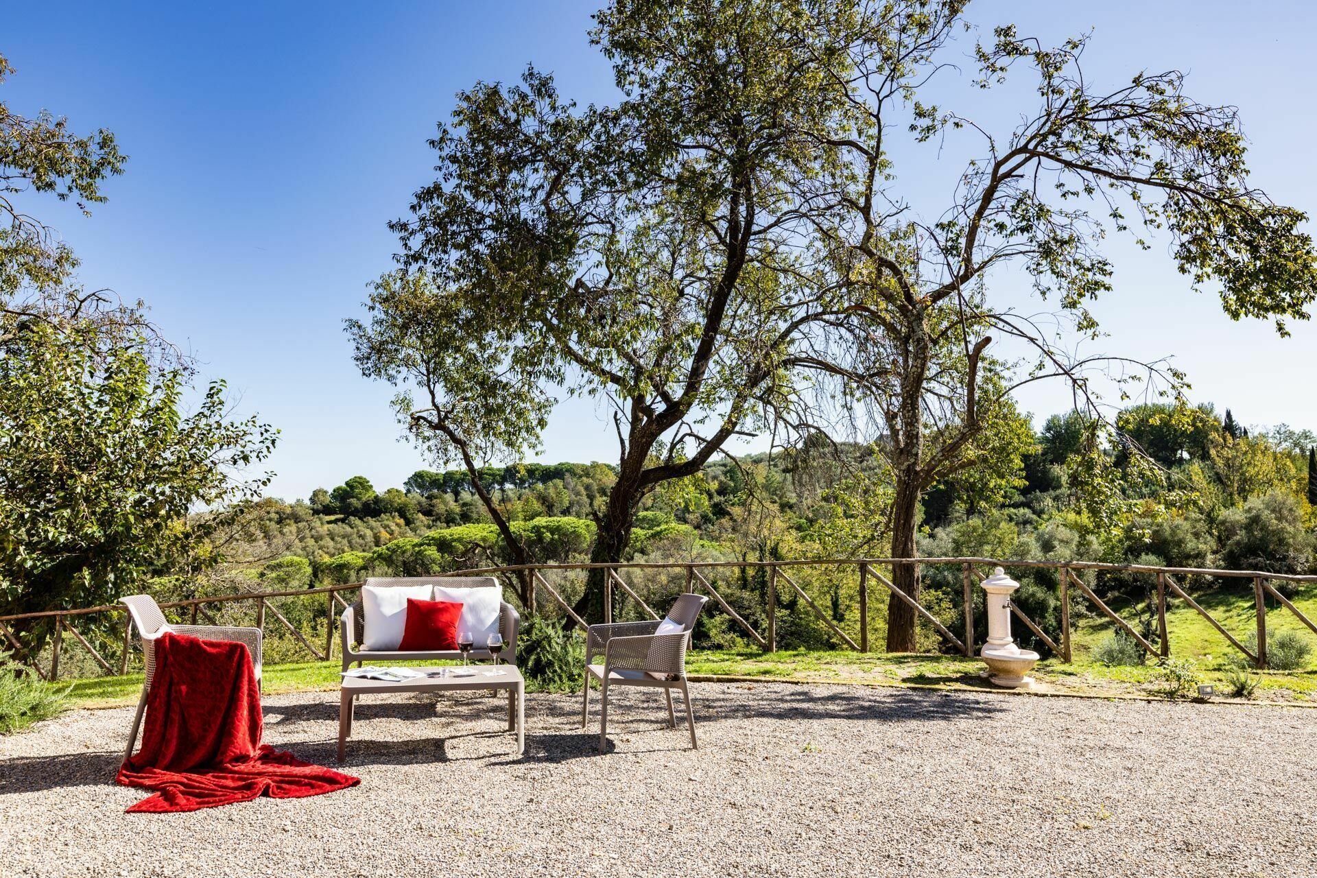 Un área de estar al aire libre con una mesa y dos sillas, una manta roja y un florero blanco.