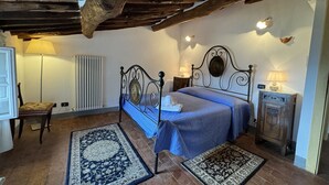 A bedroom with a bed, two rugs, a chair, a nightstand, a lamp, a radiator, and a wooden cabinet.