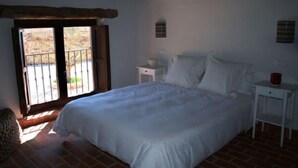 A bedroom with a bed, a nightstand, a small table, and a window with a view of the outside.