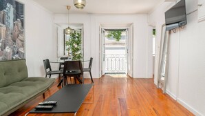 A living room with a sofa, a dining table with chairs, a TV mounted on the wall, and a balcony with a railing. - Typical Duplex Apartment in Bairro Alto (Lisboa)
