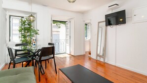 A room with a dining table, chairs, a sofa, a TV mounted on the wall, and a potted plant. - Typical Duplex Apartment in Bairro Alto (Lisboa)