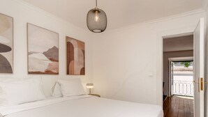 A bedroom with a large bed, a hanging light fixture, and two abstract paintings on the wall. - Typical Duplex Apartment in Bairro Alto (Lisboa)