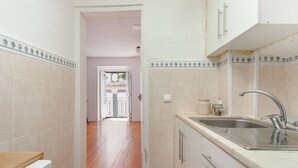A kitchen with a wooden floor, white cabinets, a stainless steel sink, and a tiled backsplash. - Typical Duplex Apartment in Bairro Alto (Lisboa)