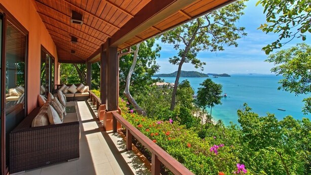 Un espacio de estar al aire libre cubierto, con vistas al mar y vegetación.