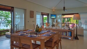 Amplia sala de estar con una mesa de comedor para cuatro personas, un sofá, una estantería y un televisor.