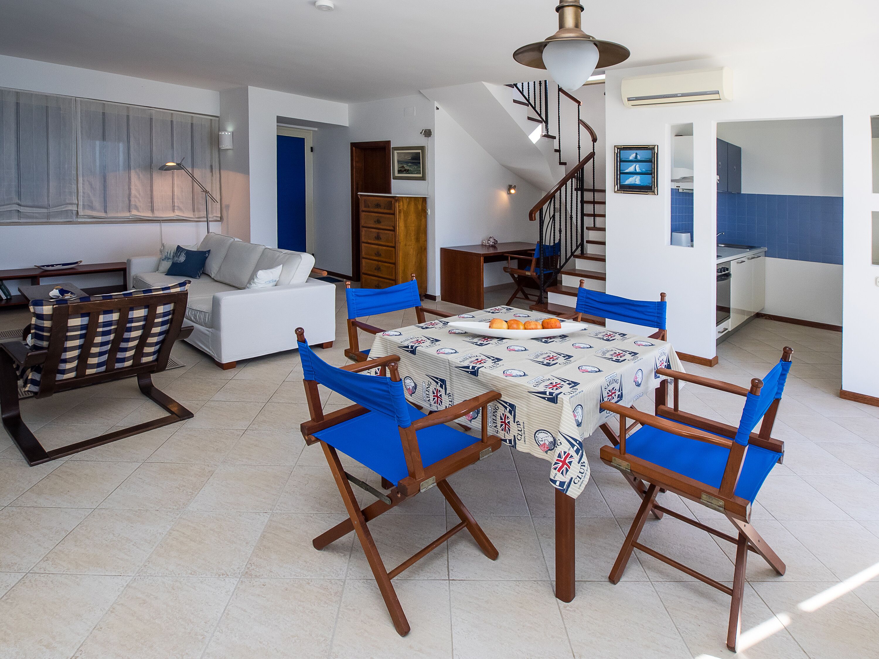Un comedor con una mesa lista para cuatro personas, un sofá y una escalera que lleva a un nivel superior.