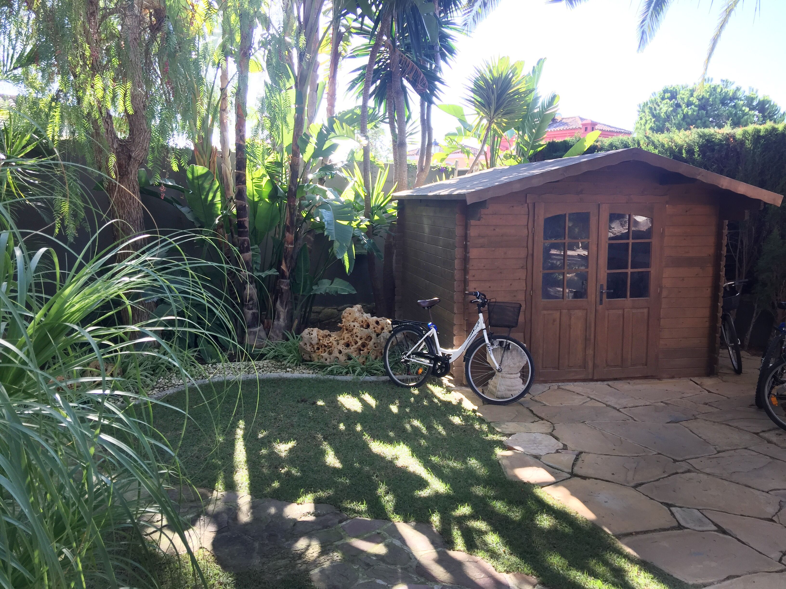 Une cabane en bois dotée d’un patio en pierre, entourée d’une végétation luxuriante et avec un vélo à proximité.