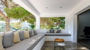 A modern living room with a built-in bench seating area, a small round table, and large windows offering a view of trees and greenery. - Modern Luxury Villa,  - 10 mins to Cala Bassa - 15 mins to Jondal/Es Torrent (San Agustín)