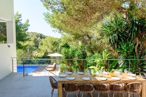 Un comedor con vista a la piscina, mobiliario exterior y plantas tropicales.