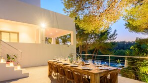 An outdoor dining area with a long wooden table set for a meal, surrounded by wicker chairs, and overlooking a pool. - Modern Luxury Villa,  - 10 mins to Cala Bassa - 15 mins to Jondal/Es Torrent (San Agustín)