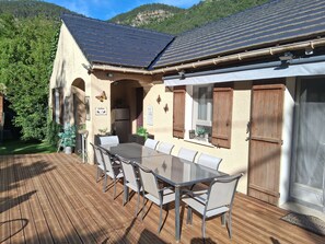 A covered outdoor dining area with a table and chairs, a refrigerator, and a window with shutters.