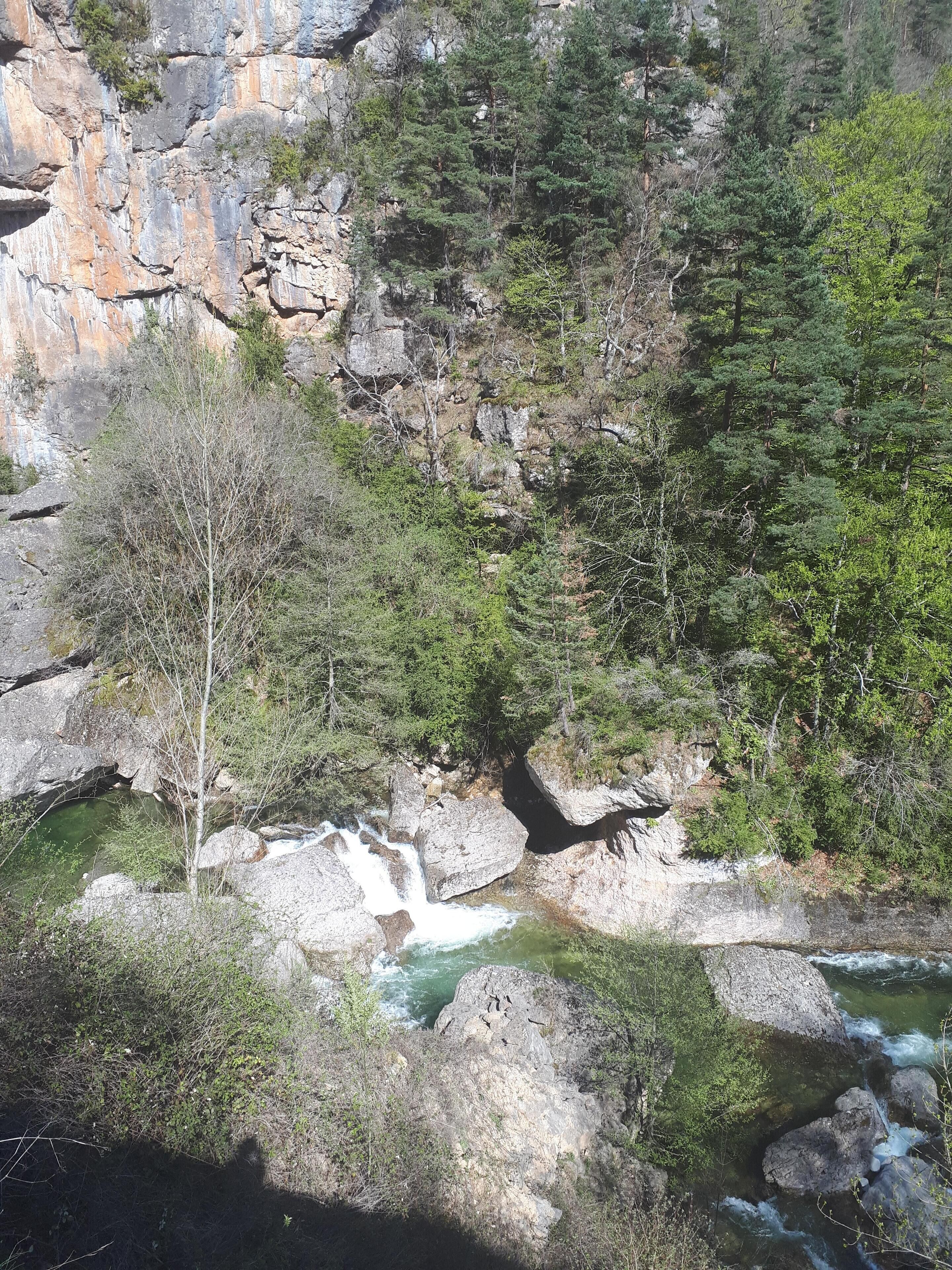A natural landscape with a waterfall, rocky terrain, and dense forest.