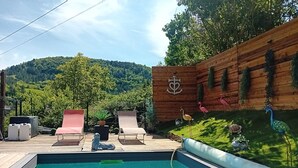A pool area with lounge chairs, a wooden deck, and a view of a forested hillside. - Riverfront house with swimming pool and magnificent view of the mountains and cliffs. (Trèves)
