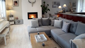 A modern living room with a grey sofa, a wooden coffee table, a fireplace, and a dining area with a bar. - Riverfront house with swimming pool and magnificent view of the mountains and cliffs. (Trèves)