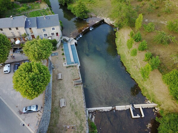 An aerial view of a riverside property with a small bridge, a solar panel, and a parking area.
